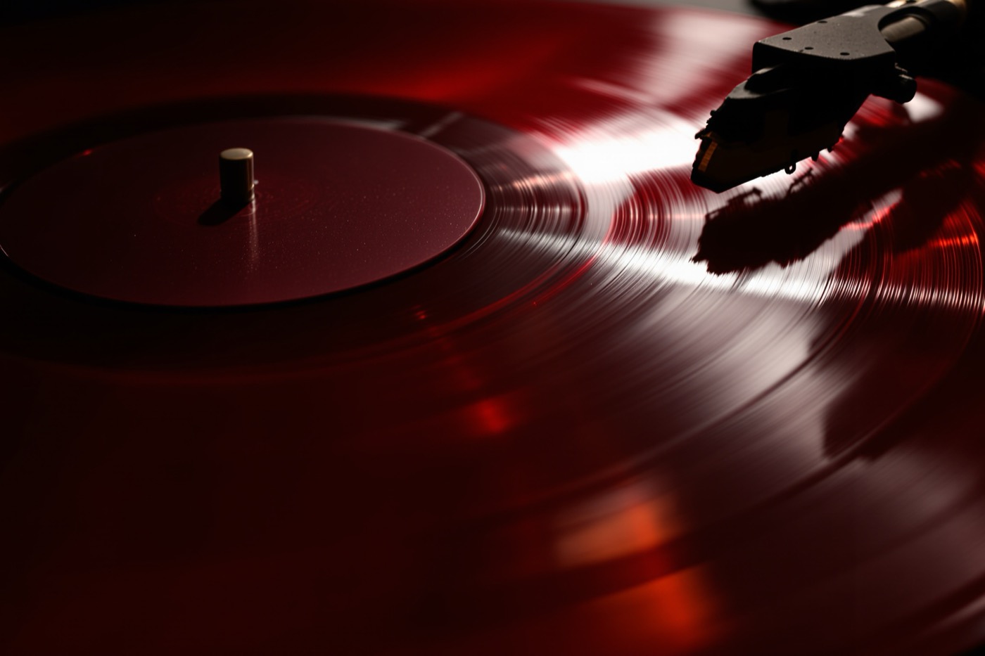 A red vinyl record turning on a turntable under one hard light, its centre label blank.
