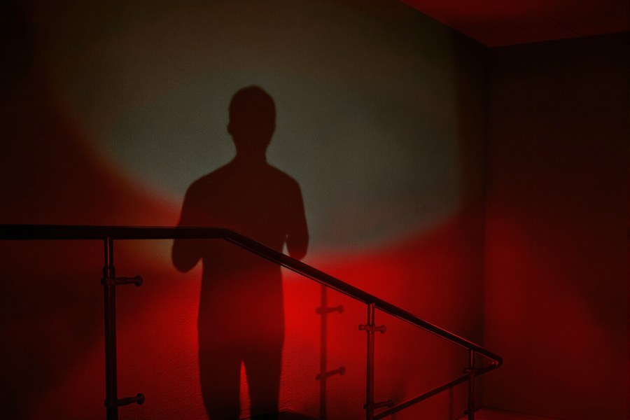 A concrete stairwell washed in red light with a long shadow on the wall.