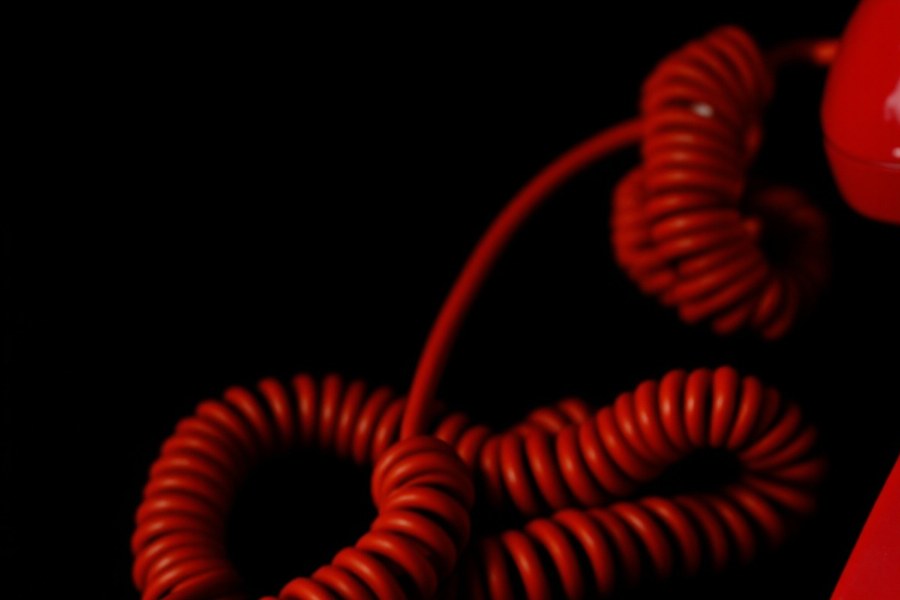 A tangled red telephone cord on a black desk, the handset off the hook.